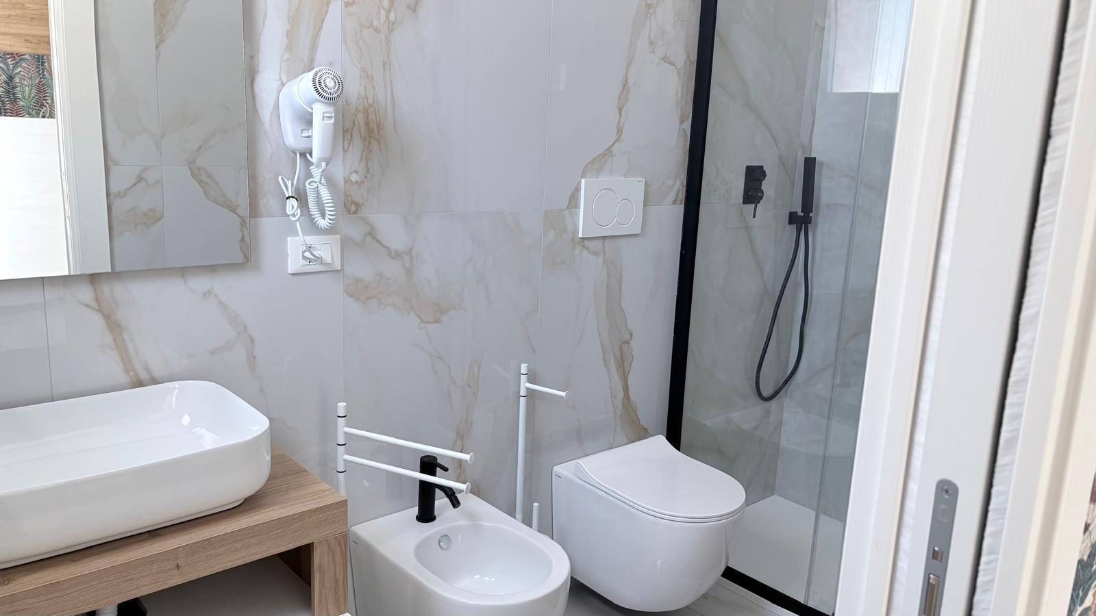 Bagno con doccia walk-in, lavandino bianco e marmo chiaro